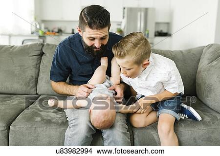 Picture - Father and boy (6-7) playing with baby boy (6-11 months) in living room. Fotosearch