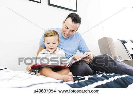 Father and son (4-5) sitting on bed and reading book View Large Photo Image Picture - Father and son (4-5) sitting on bed and reading book. Fotosearch