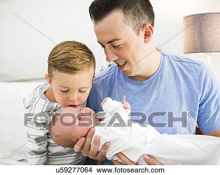 Father carrying daughter (0-1 months) and sitting on bed with son (4-5) View Large Photo Image Picture - Father carrying daughter (0-1 months) and sitting on bed with son (4-5). Fotosearch