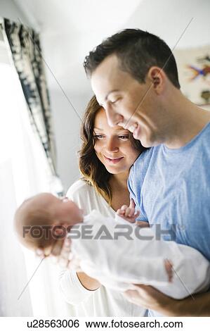Stock Photograph - Father carrying daughter (0-1 months) and standing next to mother. Fotosearch