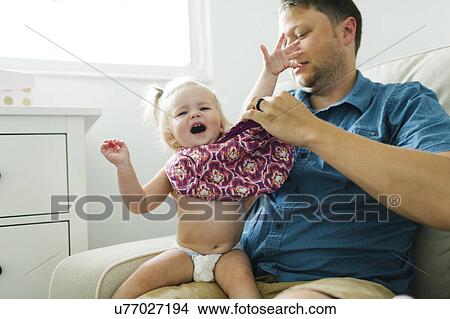 Picture - Father dressing daughter (12-17 months). Fotosearch