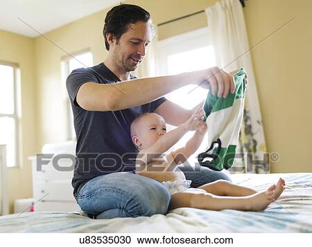 Stock Image - Father dressing son (12-17 months) in bedroom. Fotosearch