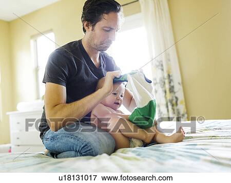 Stock Photo - Father dressing son (12-17 months) in bedroom. Fotosearch