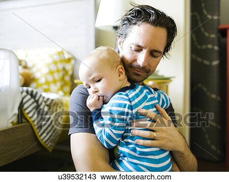 Stock Image - Father embracing baby boy (12-17 months) in bedroom. Fotosearch