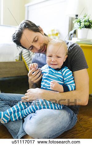 Stock Photo - Father embracing sad son (12-17 months). Fotosearch