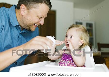 Stock Image - Father feeding baby girl (12-17 months). Fotosearch