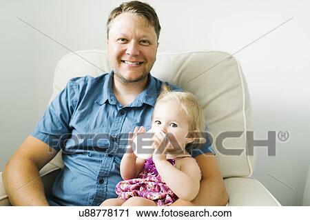 Stock Image - Father feeding baby girl (12-17 months) in living room. Fotosearch