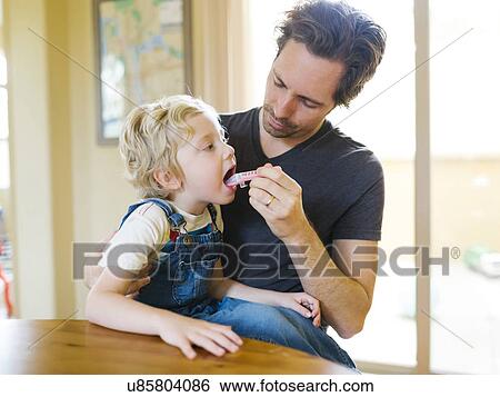Stock Photograph - Father giving son (4-5) antibiotic. Fotosearch