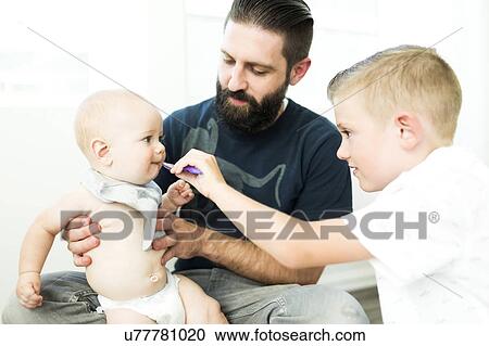 Stock Image - Father looking at boy (6-7) feeding brother (6-11 months). Fotosearch