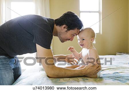 Stock Image - Father playing with baby boy (12-17 months) in bedroom. Fotosearch