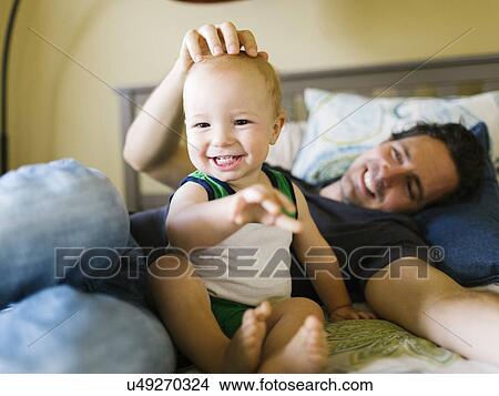 Picture - Father stroking baby boy (12-17 months) in bedroom. Fotosearch