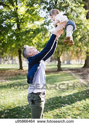 Picture - Father throwing daughter (12-17 months) up in air in park. Fotosearch