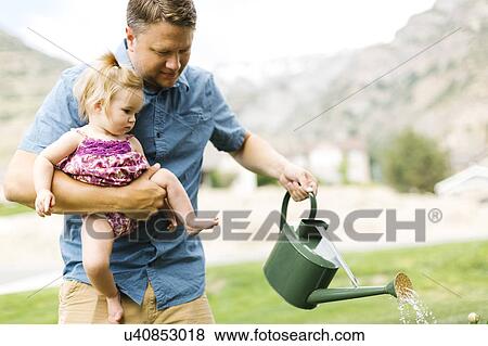 Stock Photo - Father with baby girl (12-17 months) watering plants in backyard. Fotosearch