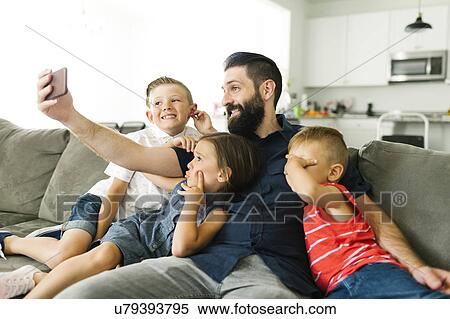 Stock Photography - Father with his three children (2-3, 6-7) taking selfie with smart phone. Fotosearch