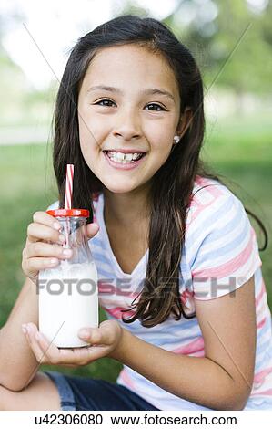 Stock Image - Girl (10-11) in park holding glass of milk with straw. Fotosearch