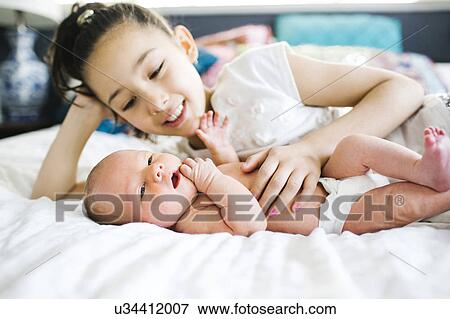Stock Photo - Girl (10-11) lying in bed beside brother (2-5 months). Fotosearch