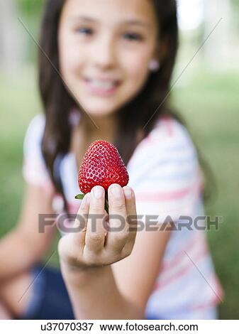 Girl (10-11) presenting strawberry View Large Photo Image Stock Photo - Girl (10-11) presenting strawberry. Fotosearch