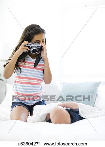 Girl (10-11) taking photo of her small brother (12-17 months) lying on bed View Large Photo Image Stock Image - Girl (10-11) taking photo of her small brother (12-17 months) lying on bed. Fotosearch