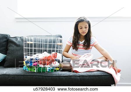 Stock Image - Girl (10-11 ) with laundry sitting on sofa. Fotosearch
