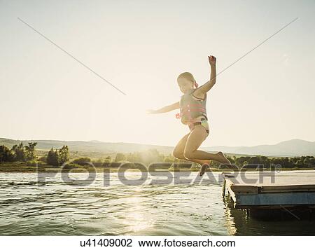 Stock Image - Girl (4-5) jumping into lake from pier. Fotosearch