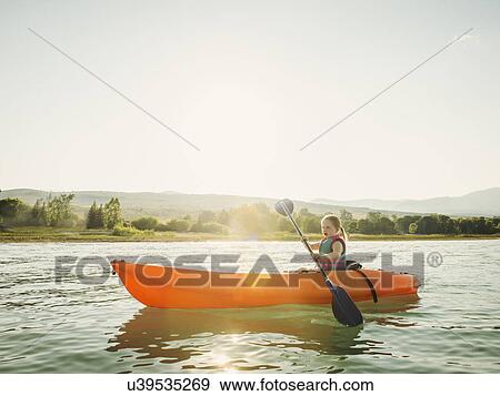 Stock Photo - Girl (4-5) kayaking on lake at sunset. Fotosearch