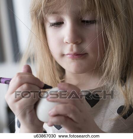 Stock Image - Girl (4-5) making colored Easter eggs. Fotosearch