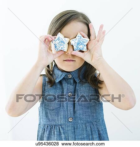 Stock Photo - Girl (6-7) holding cookies in front of eyes. Fotosearch