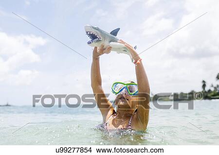 Picture - Girl (6-7) playing with shark toy in sea. Fotosearch