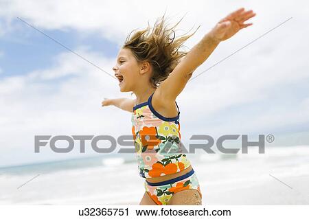 Stock Image - Girl (6-7) spinning on beach. Fotosearch