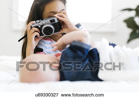 Girl(10-11) taking photo of her small brother (12-17 months) lying on bed View Large Photo Image Stock Photo - Girl(10-11) taking photo of her small brother (12-17 months) lying on bed. Fotosearch