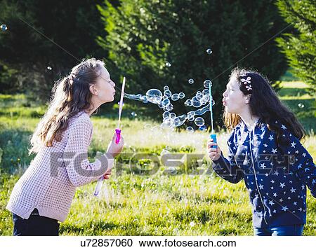 Stock Image - Girls (10-11, 12-13) blowing bubbles in field. Fotosearch