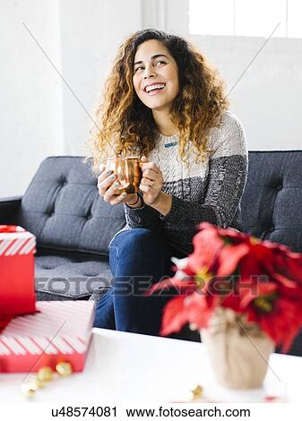 Happy woman on sofa, holding mug with Christmas gifts in foreground View Large Photo Image Stock Image - Happy woman on sofa, holding mug with Christmas gifts in foreground. Fotosearch