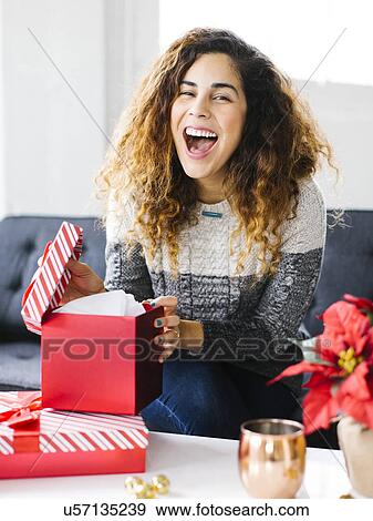 Stock Photo - Happy woman on sofa opening Christmas gift. Fotosearch
