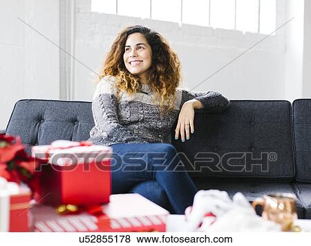 Stock Photo - Happy woman on sofa with Christmas gifts in foreground. Fotosearch