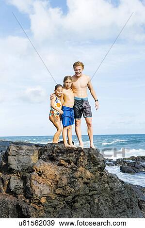 Stock Photo - Man and children (6-7, 8-9) standing on rock by sea. Fotosearch