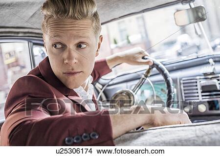 Picture - Man driving vintage car, looking over shoulder. Fotosearch