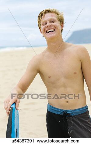 Stock Image - Man standing on beach and holding surfboard. Fotosearch