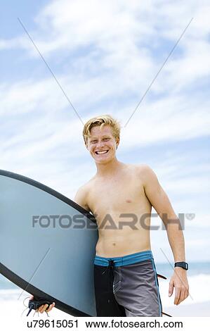 Stock Image - Man standing on beach and holding surfboard. Fotosearch