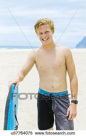 Man standing on beach and holding surfboard View Large Photo Image Stock Photography - Man standing on beach and holding surfboard. Fotosearch