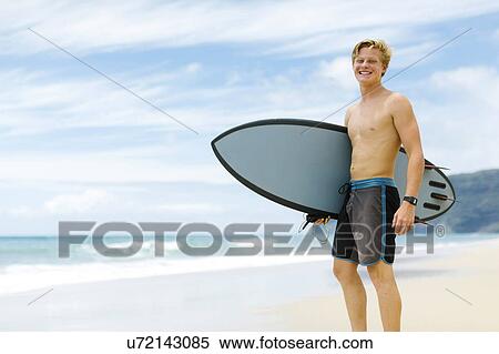 Man standing on beach and holding surfboard View Large Photo Image Stock Photography - Man standing on beach and holding surfboard. Fotosearch