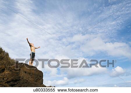 Man standing on rock against blue sky View Large Photo Image Stock Photography - Man standing on rock against blue sky. Fotosearch