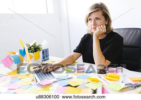 Stock Image - Mature woman at office overwhelmed by adhesive notes. Fotosearch