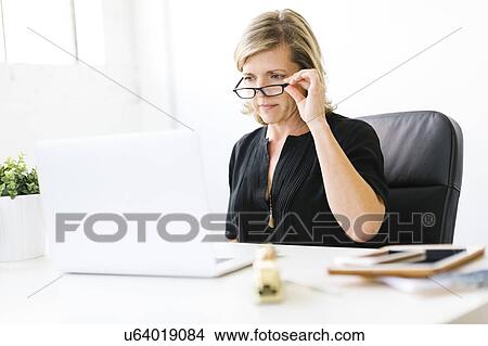 Mature woman in office touching her eyeglasses View Large Photo Image Picture - Mature woman in office touching her eyeglasses. Fotosearch