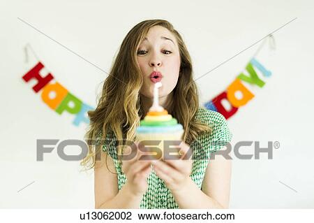 Stock Image - Mid adult woman blowing birthday candle. Fotosearch