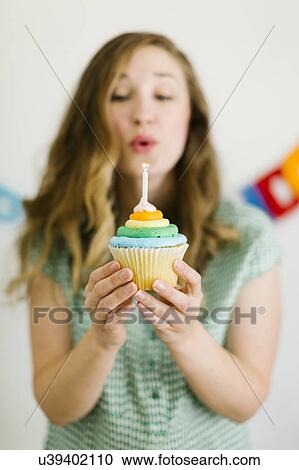 Stock Image - Mid adult woman blowing birthday candle. Fotosearch