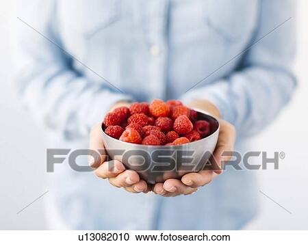 Stock Image - Mid section of Mature woman holding bowl with raspberries. Fotosearch