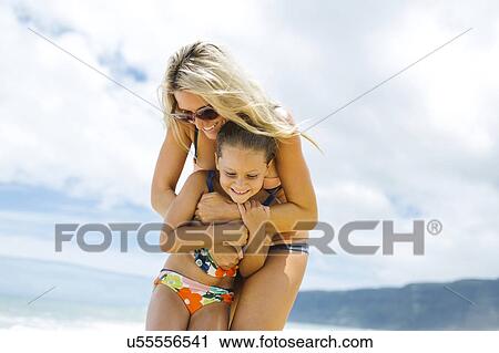 Stock Image - Mother and daughter (6-7) embracing on beach. Fotosearch