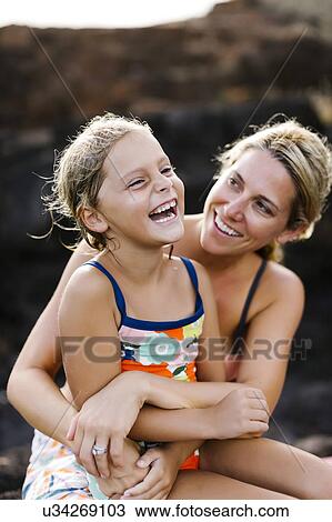 Stock Image - Mother and daughter (6-7) embracing with rock in background. Fotosearch