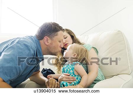 Stock Photography - Mother and father with baby girl (12-17 months) sitting in living room and kissing. Fotosearch