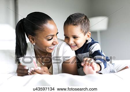 Picture - Mother and son (2-3) lying on bed and using smart phone. Fotosearch